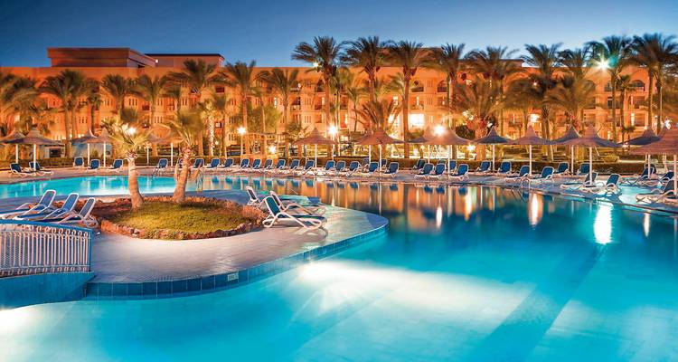 Resortpool bei Nacht mit Palmen und beleuchteten Gebäuden.