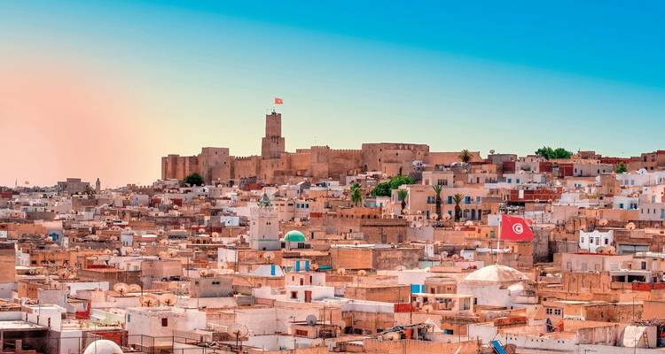 Panoramic view of the Medina of Sousse with a fort in the distance and flags waving.