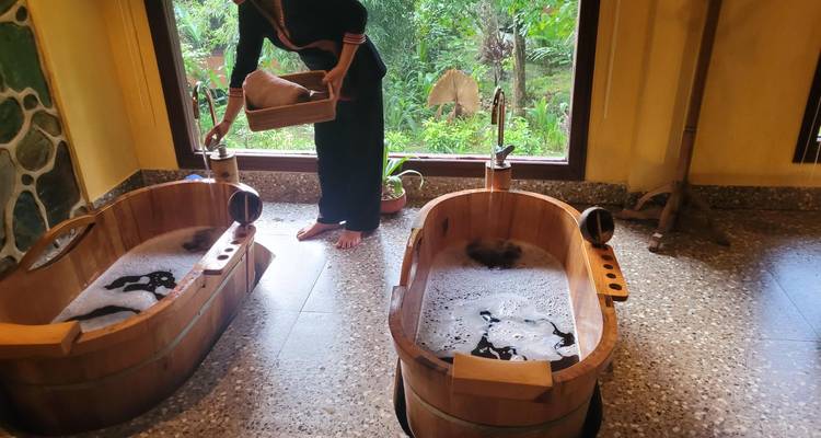 Attendant prepares steaming herbal wooden bathtubs beside a garden view window.