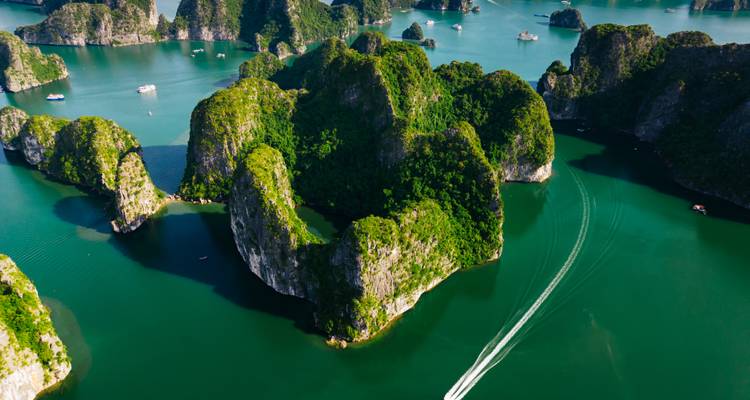 Stunning aerial of emerald karst islands and boats leaving white wakes through Ha Long Bay waters.