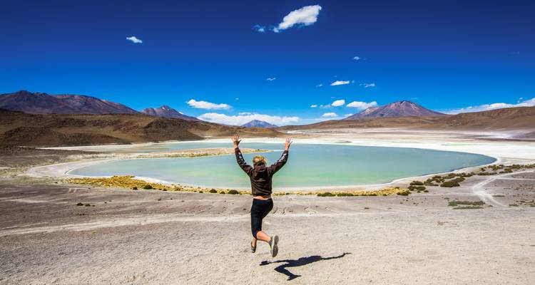 Opgewonden reiziger springt met geheven armen uit over het turkooizen water van de Laguna Verde.