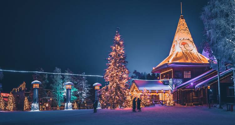 Festlich beleuchtetes Weihnachtsmanndorf mit verschneiter Landschaft bei Nacht.