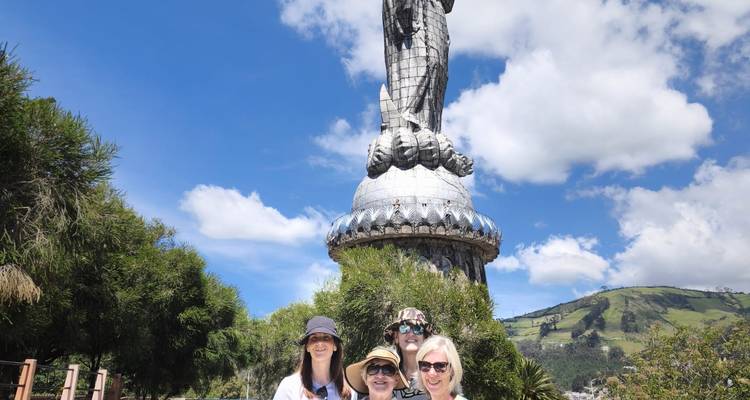 Four women smile in front of Quito’s towering Virgin of El Panecillo statue with blue skies overhead.