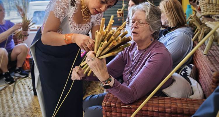 A local instructor helps a visitor weave reeds during a traditional craft workshop.
