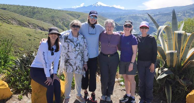 Travellers pose with a snow-capped volcano in the distance amid green Andean hills.
