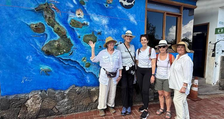 A group of women stand beside a colourful mural map of the Galápagos Islands.