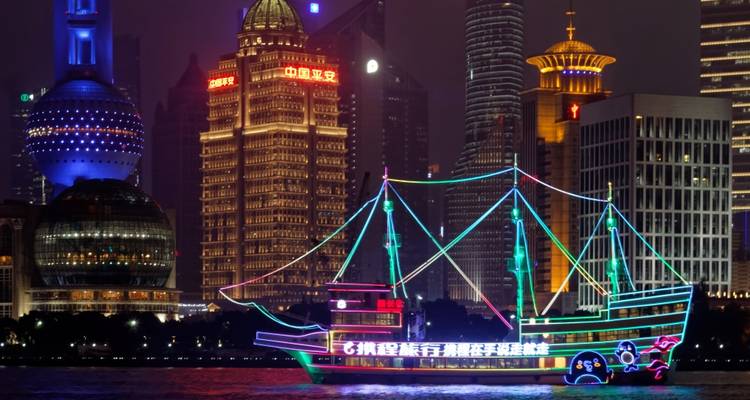 Barco iluminado con neón en un río contra un horizonte de edificios iluminados.