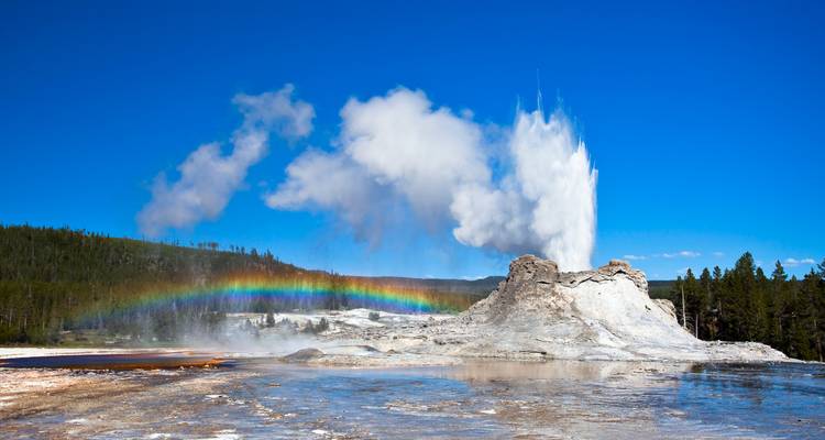 Geyser Old Faithful en éruption avec un arc-en-ciel dans l'embruns.