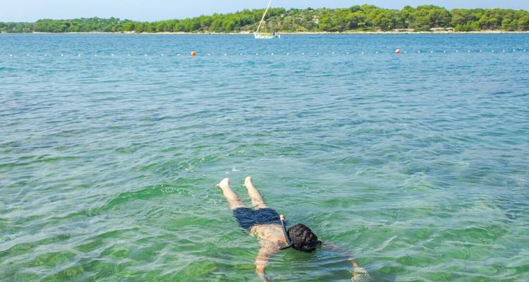 Personne faisant de la plongée avec tuba dans une eau claire avec un bateau au loin.