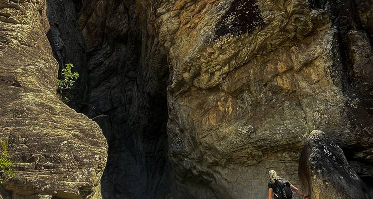 Wanderer, der von hohen dunklen Canyonwänden aus verwittertem Granit überragt wird.