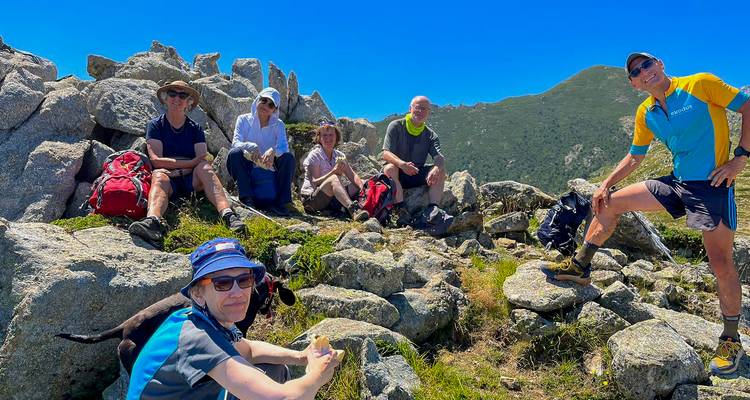 Gruppe von Wanderern, die sich auf Felsbrocken auf einem Berggipfel mit blauem Himmel über ihnen ausruhen.