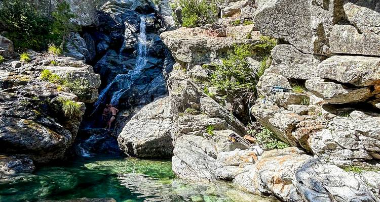 Klarer Felsenpool an der Basis eines kleinen Wasserfalls in einer bewaldeten Schlucht mit einem Badegast, der das Wasser genießt.