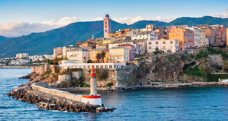 Farbenfrohe, an der Klippe gelegene Stadt Bastia mit Leuchtturm und Wellenbrecher, die sich bei Sonnenuntergang ins Meer erstrecken.