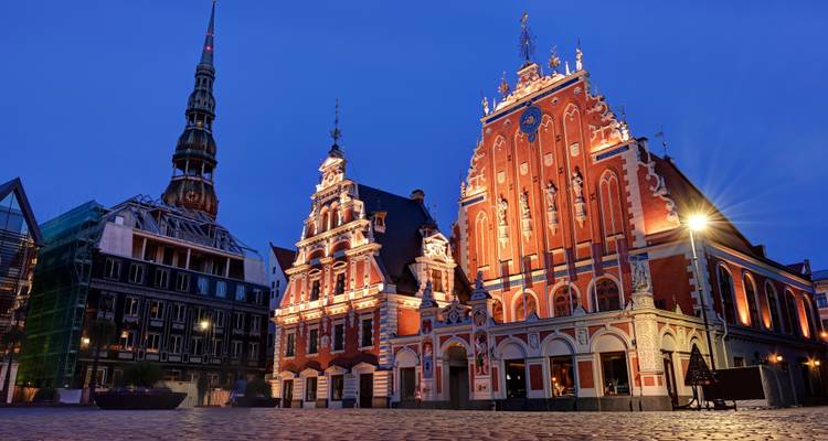 Dramatisch nachtelijk uitzicht op Riga's Huis van de Zwartkoppen en de prachtig verlichte Sint-Pieterskathedraal.