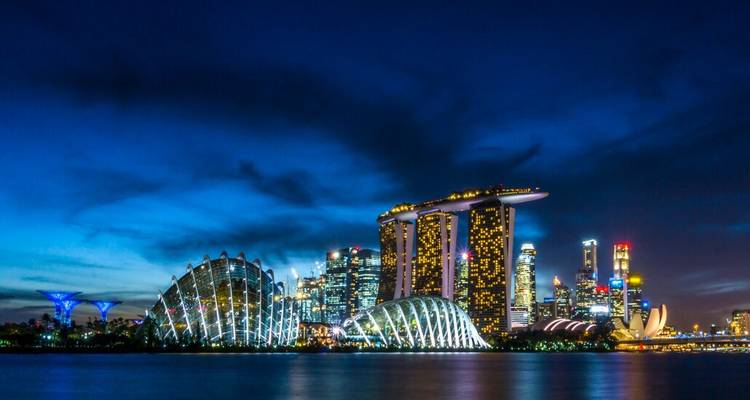 Singapore’s glittering skyline at night with Marina Bay Sands and Supertrees lit against a deep blue sky.