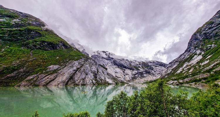 Lago glacial de verde esmeralda que refleja acantilados grises y empinados bajo cielos dramáticos llenos de nubes.