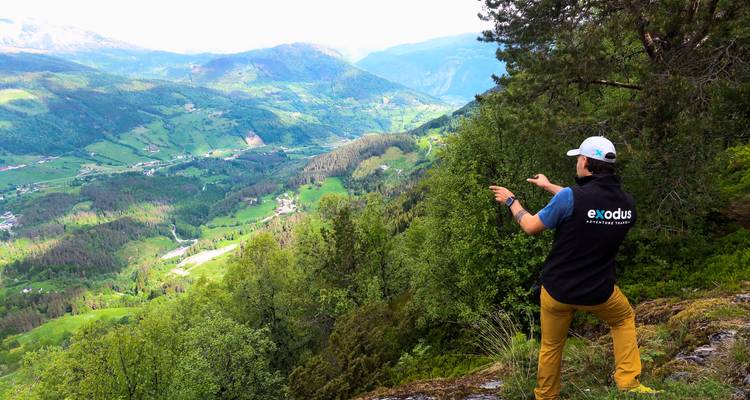 Un guía señala con la mano hacia un amplio valle noruego lleno de bosques, granjas y picos distantes.