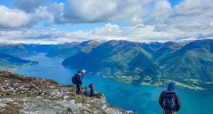 Des randonneurs se tiennent au sommet rocheux et contemplent les vues étendues d'un fjord bleu qui serpente à travers les montagnes.