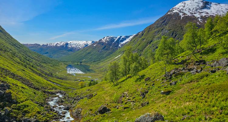 Une vallée verdoyante avec une cascade mène à un lac aux eaux tranquilles entouré de pics ondulants.
