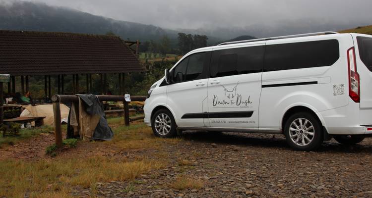 Tour vehicle parked on a gravel track in misty rural surroundings near pine-clad hills.
