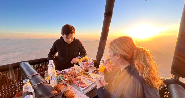 Un groupe prenant le petit-déjeuner dans une montgolfière au lever du soleil.