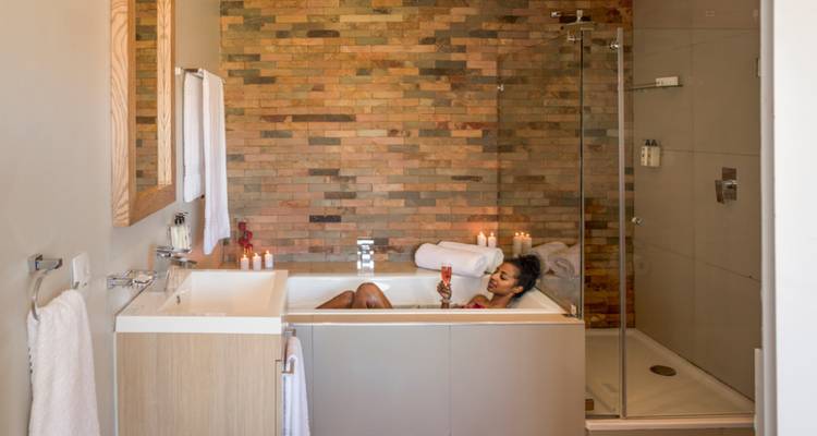 Una persona relajándose en una bañera moderna con velas y una bebida.