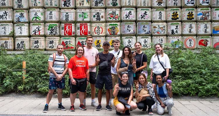 Group of people standing in front of colorful barrels with Japanese writing.