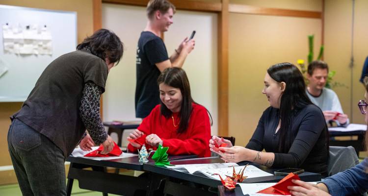Group of people engaged in an Origami lesson in a traditional room.