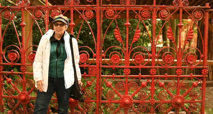A smiling traveler poses in front of an ornate red wrought-iron gate surrounded by greenery.