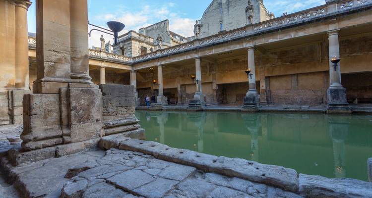 Historic Roman Baths in Bath with green thermal water surrounded by ancient stone columns and visitors observing the pool.