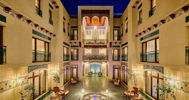 Eleganter Hotelinnenhof bei Nacht mit kunstvollen Fliesen, Balkonen und warmer Beleuchtung um einen zentralen Sitzbereich