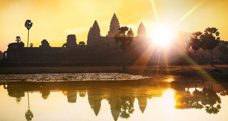 Silhouetten van torens van Angkor Wat weerspiegeld in een rustige vijver bij zonsopgang met gouden lichtstralen.