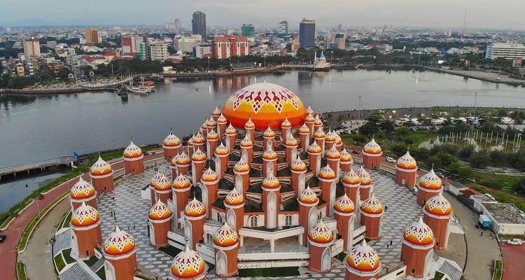 Vista con dron de la impresionante mezquita con cúpula naranja y numerosas torres que domina una ciudad costera.