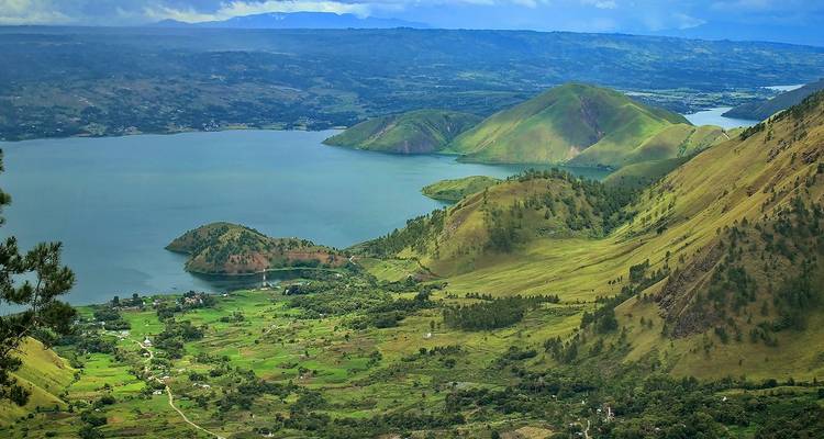 Vue panoramique du lac Toba avec des péninsules luxuriantes, des îles et des vallées vertes en mosaïque.