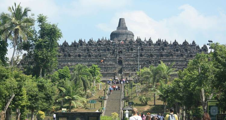 Visitors climbing the central staircase of the vast stone Borobudur temple surrounded by greenery