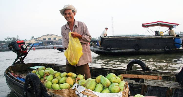 Floating market vendor with tropical fruits on a boat.