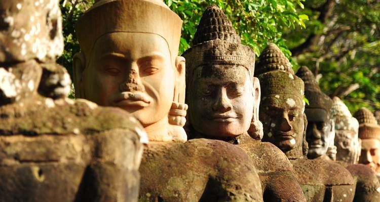 Rij van oude stenen wachterstatues bij Angkor Thom omringd door jungle-begroeiing.