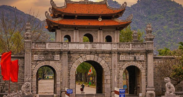 Puerta de piedra de la antigua capital Hoa Lu con montañas de fondo y un visitante solitario caminando a través de ella.