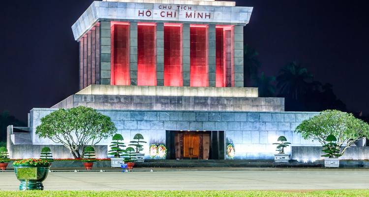 Vista nocturna del Mausoleo de Ho Chi Minh iluminado con luces rojas y blancas.