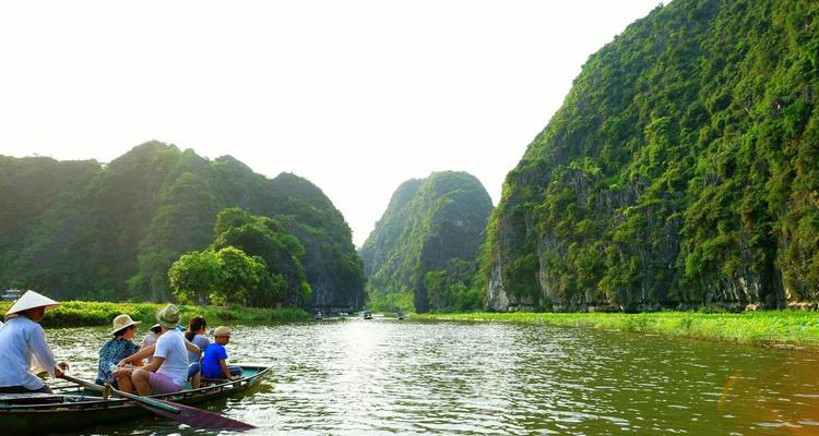 Travelers sit in a small wooden boat gliding along a calm river between towering limestone karsts.