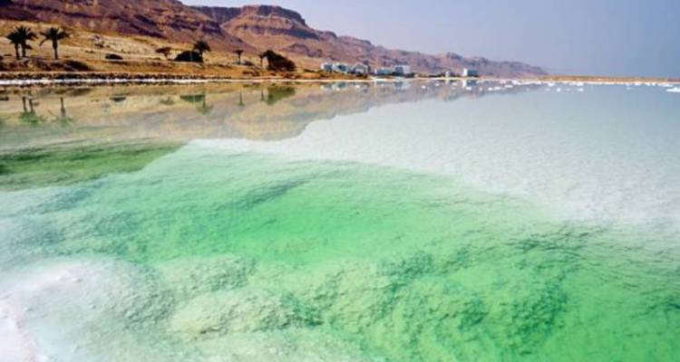 Blick auf das Tote Meer mit türkisfarbenem Wasser und umliegendem Land.