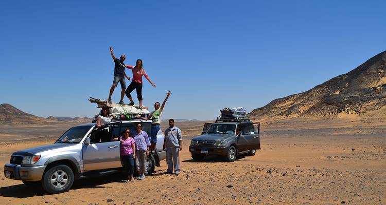 Grupo de personas en un safari por el desierto con dos SUVs en un paisaje arenoso.