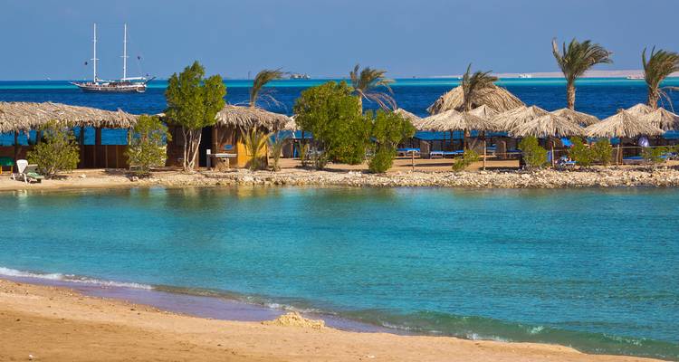 Tropischer Strand mit Hütten und Palmen am türkisfarbenen Meer.
