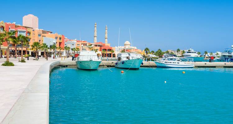 Marina with boats docked next to colorful buildings and clear blue water.