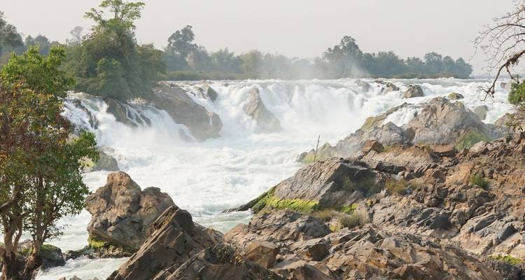 Una poderosa cascada de múltiples niveles que cae estrepitosamente sobre salientes rocosos hacia un amplio río