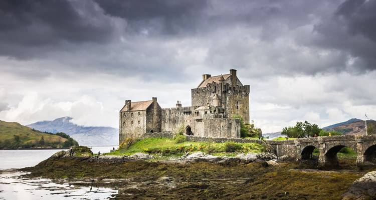 El histórico Castillo de Eilean Donan se alza en su isla de mareas enmarcado por cielos sombríos y lejanas colinas de las Tierras Altas.