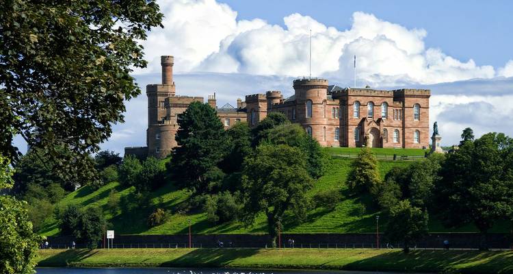 El Castillo de Inverness corona una colina verde sobre el río Ness con nubes esponjosas llenando el cielo de verano.