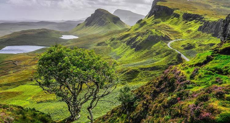 Dramatische grüne Grate und gewundene einspurige Straße der Quiraing-Landschaft auf der Isle of Skye unter aufgelockertem Wolkenbestand.