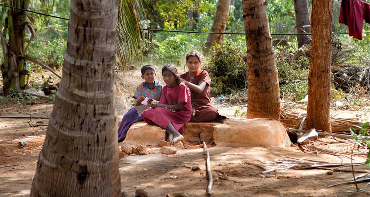 Three children sitting on a stone bench surrounded by trees.