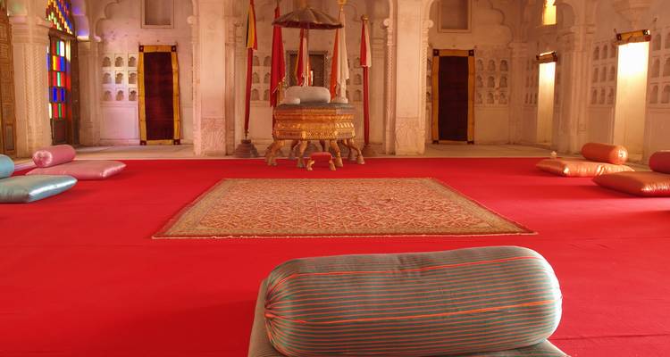 Interior de un palacio con alfombras rojas y cojines.